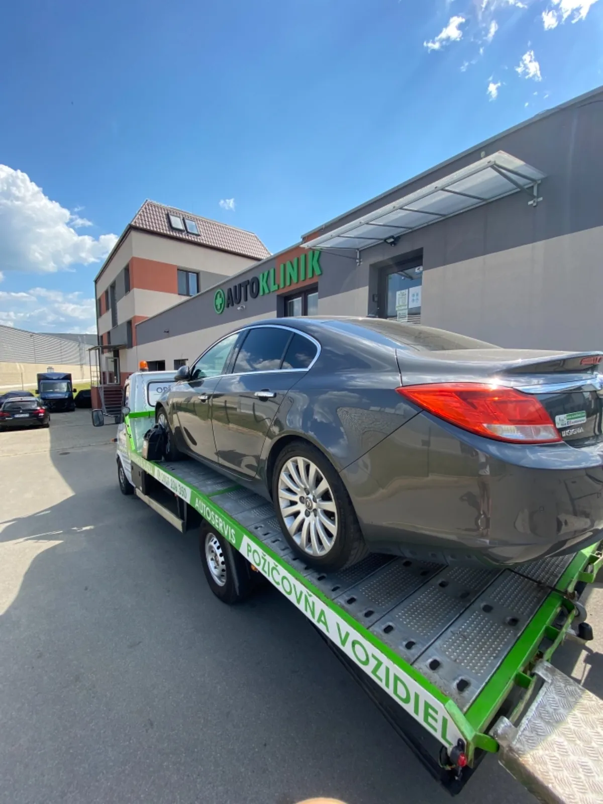 Osobné auto na autoprepravníkovom prívese pred budovou servisu